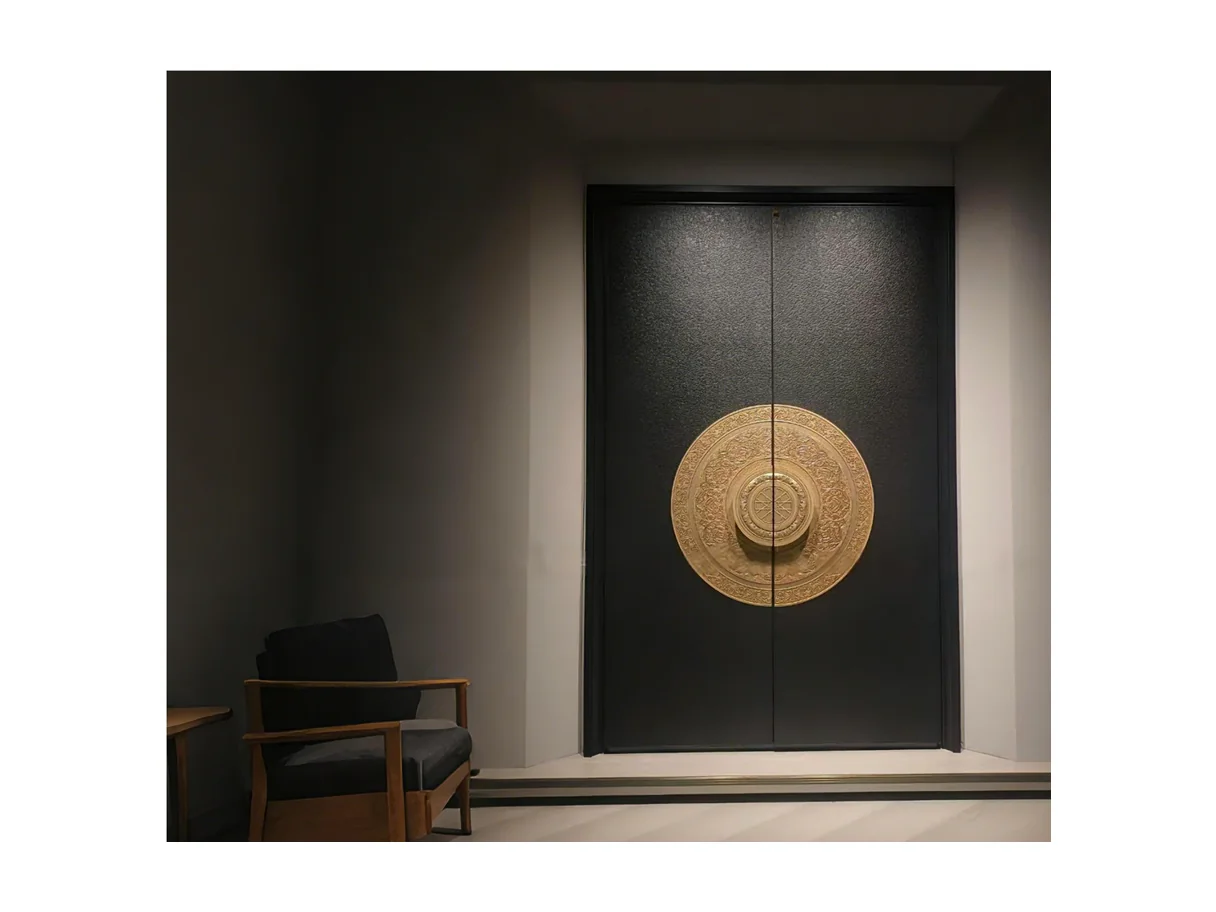 Front view of a dark aluminium entrance leaf with a large circular brass disc ornament and glazed flanking panes