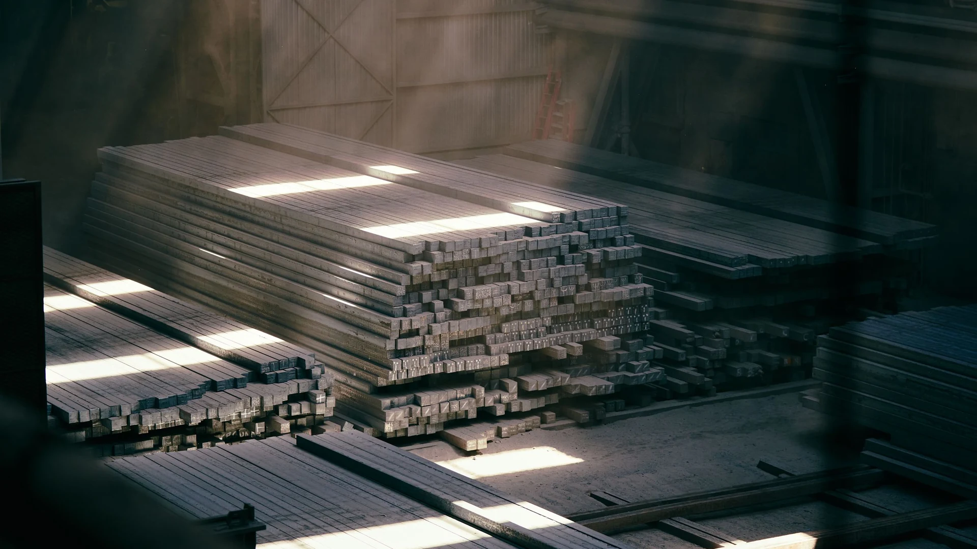 Bundles of extruded aluminium square profiles stacked on pallets inside the production hall